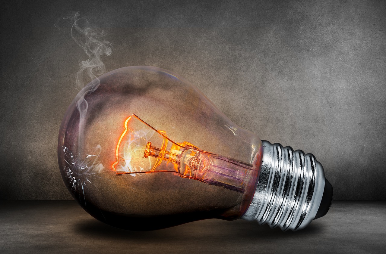 Close-up of a broken incandescent light bulb on a dark surface with smoke and a glowing filament, symbolizing energy failure or burnout.
